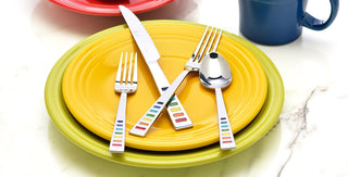 Sliver forks, knives, and spoons with Fiesta rainbow colors on the flatware. This flatware is on two yellow plates
