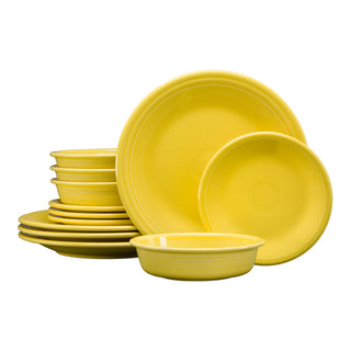 A set of yellow ceramic dinnerware, including plates and bowls, is stacked together on a white background. The pieces are round with simple, smooth edges.