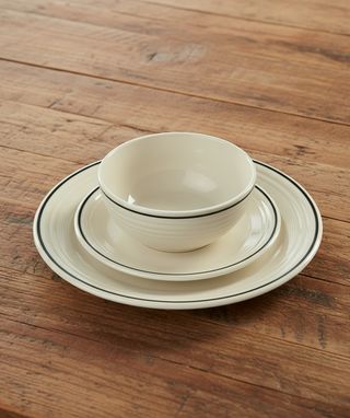A white bowl, small plate, and large plate with thin black rims are stacked on top of each other on a wooden table.