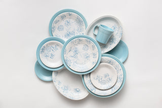 A collection of blue and white floral-patterned plates arranged in a circular pattern with a light blue mug placed on top, all set against a white background.