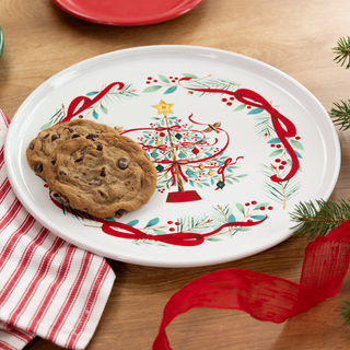 Two chocolate chip cookies on a white plate decorated with a Christmas tree and red ribbon design.