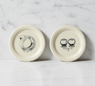 Two cream-colored Fiesta Icons coasters feature Disk Pitcher and Salt and Pepper Set designs, each with a handwritten-style label for added charm; set includes two 4 3/8 inch covers from Fiesta.
