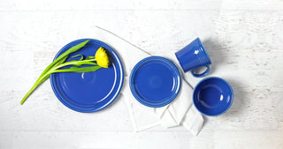 A white tabletop with 2 lapis (blue) colored plates, 1 mug, and 1 bowl.