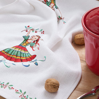 The Town and Country Nutcracker Ballerina Holiday Holly Sprig Kitchen Towel Set features white textured cotton towels with a festive ballerina and holly design—ideal for holiday decor, shown alongside walnuts and a red mug on a wooden surface.