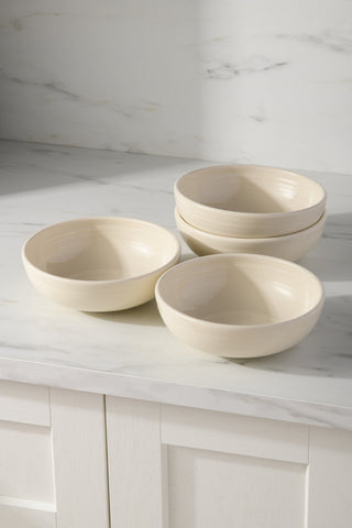 Four Fiesta FTC Linen Bistro Coupe 7 5/8-Inch 38oz Medium Bowls are stacked on a white marble counter. These lead-free ceramic bowls come in a set of four, are dishwasher safe, and softly lit by sunlight against light cabinetry.