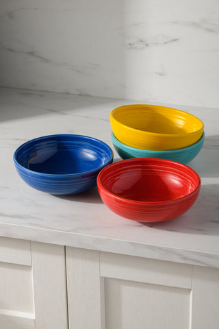 The Fiesta (FTC) Mixed Vibrant Bistro Coupe 7 5/8-Inch 38OZ Medium Bowls, Set of 4, features blue, red, yellow, and green bowls displayed on a white marble countertop above white cabinet drawers.