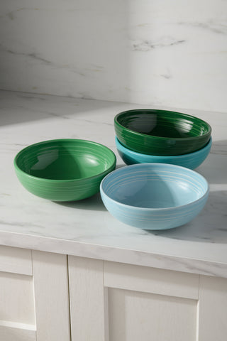 The Fiesta Mixed Aegean Bistro Coupe 7 5/8-Inch 38OZ Medium Bowls, Set of 4, features ceramic bowls in green and blue stacked on a white marble countertop with white cabinets. All are dishwasher safe for easy cleanup.