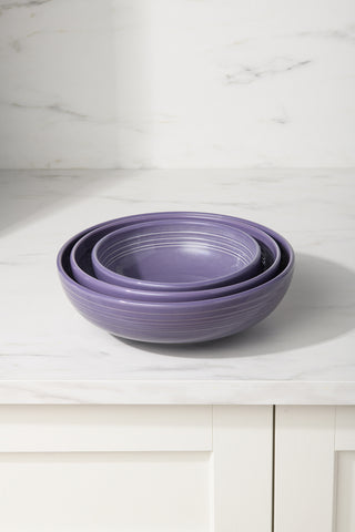 Three nested lavender ceramic bowls, including the Fiesta Lavender Bistro Coupe 10 1/2 Inch Extra Large Bowl (96 oz), sit on a white marble countertop with a white cabinet and light marble backsplash in the background.