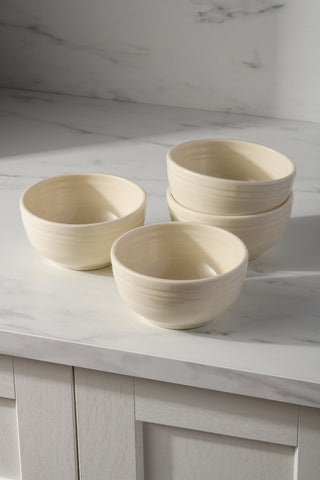 The Fiesta (FTC) Linen Bistro Coupe 5 1/2 Inch Cereal Bowl 22 oz Set of 4 features four cream-colored bowls, perfect for adding elegance and function to your dining essentials. Ideal for cereal or snacks, they're shown stacked on a marble countertop in a bright kitchen.