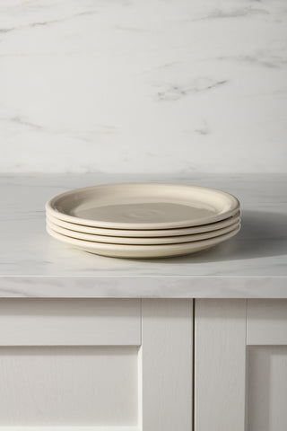 A set of 4 Fiesta (FTC) Linen Bistro Coupe 10 1/2 Inch Dinner Plates is stacked on a white marble countertop, with white paneled cabinets and a matching marble backsplash in the background.