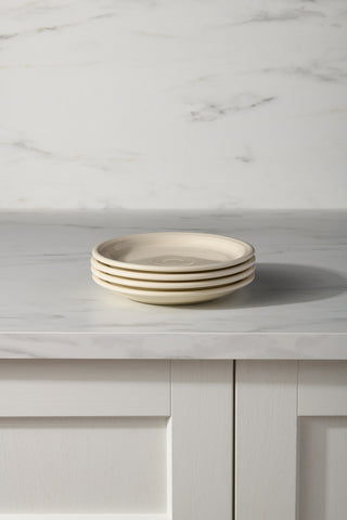 A set of four Fiesta (FTC) Linen Bistro Coupe 7 1/4 Inch Salad Plates is stacked on a light marble countertop, with white paneled cabinetry and a marble-patterned wall in the background.