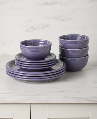 The Fiesta Lavender Bistro Coupe 12-Piece Dinnerware Set, Service for 4, is stacked neatly on a white marble countertop above a light-colored cabinet, featuring ceramic plates and bowls in a stylish lavender hue.