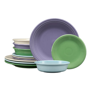 The Lavender Bloom Mixed Color Classic Rim 12-Piece Dinnerware Set by Fiesta Factory Direct features pastel-hued ceramic dishes in purple, green, cream, and blue, stacked in neat piles against a white background.