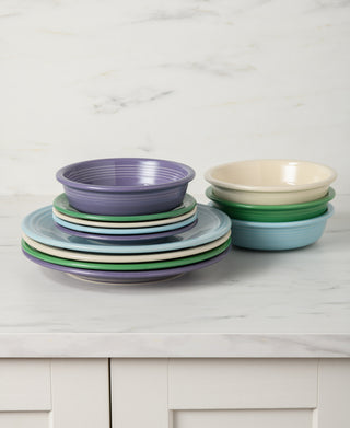 Stacks of colorful ceramic plates and bowls, including the Fiesta Lavender Bloom Mixed Color Classic Rim 12-Piece Dinnerware Set (Service for 4), are neatly arranged on a white marble countertop against a light marble backdrop.