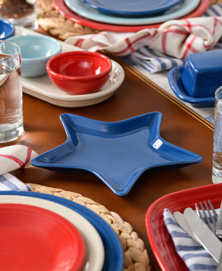 The Fiesta Star Plate adds a festive touch to your table, surrounded by red, blue, and white lead-safe china, water glasses, cutlery, and striped napkins. Ideal as a hostess gift!.