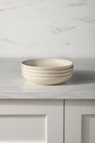 A stack of four Fiesta Linen Coupe 8 1/2 Inch Luncheon Bowls (26 oz) sits on a white marble countertop with white paneled cabinets and a marble backsplash, perfect for serving salads or pasta.