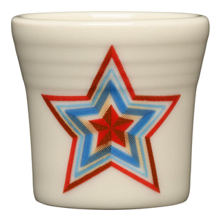 The Fiesta (FTC) Americana Scarlet Faceted Star 1 1/2 OZ ceramic shot glass, made in the USA, is cream-colored and features a multicolored layered star with red, blue, tan, and black outlines on one side.