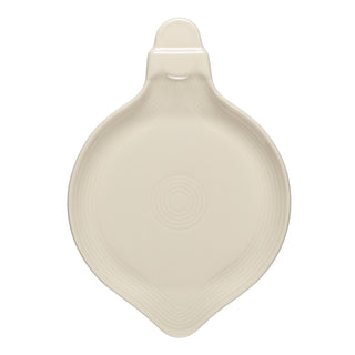 A cream-colored ceramic spoon rest with a rounded base, a small handle at the top, and concentric circular designs in the center.
