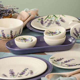 A set from the Lavender Bloom Collection features ceramic dishes adorned with lavender flower designs—plates, bowls, and small dishes—arranged on a table with a purple tray, napkins, and a bundle of dried lavender. The ensemble includes the Fiesta Lavender Bloom 3 3/4 Inch Mini Bowl 5 OZ for added charm and versatility.