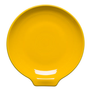 The Fiesta New Retired Extra Large Spoon Rest 7 Inch is a round, bright yellow ceramic utensil holder with a tab-like extension and subtle concentric circle patterns, shown on a white background.