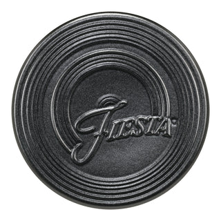 The Fiesta (FTC) Foundry Extra Large Trivet, 8 1/4 inch, is a round black ceramic trivet with concentric raised rings and “Fiesta” embossed in cursive—perfect for protecting surfaces from heat.