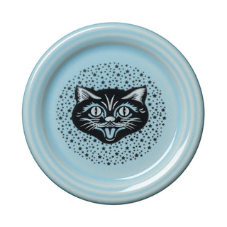 The Fiesta Black Cat Sky 4 3/8 Inch Coaster and Mug Cover, made in the USA from vitrified china, showcases a black and white cartoon cat face at its center, encircled by small black stars on a light blue background. Combining playful design with lasting durability, this dishwasher safe accessory is perfect for adding charm to your table.