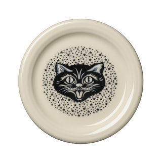 The Fiesta Black Cat Linen 4 3/8 Inch Coaster and Mug Cover is crafted from vitrified china with a cream-colored finish. It showcases a playful black illustration of a cat’s head sticking out its tongue, encircled by a ring of small black stars. This dishwasher-safe accessory is proudly made in the USA.