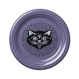 The Fiesta Black Cat Lavender 4 3/8 Inch Coaster and Mug Cover, made in the USA from durable vitrified china, features a playful black and white cartoon cat face with wide eyes and an open mouth, surrounded by a circle of small black stars. This dishwasher-safe accessory combines lasting durability with whimsical design.