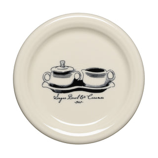 A cream-colored plate from Fiesta features a black illustration of a sugar bowl and creamer set on a tray. Below the drawing, “Sugar Bowl & Creamer 1940” is written in cursive, celebrating classic Fiesta Icons. Crafted from lead-safe china, this piece is part of the Fiesta Icons Medium Vase and Sugar Bowl and Creamer Set with Tray collection.