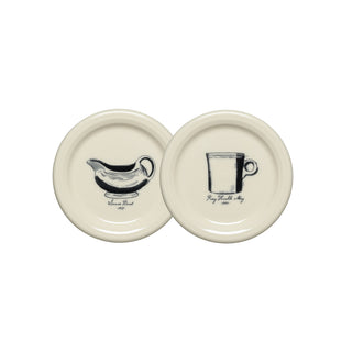 Set of two cream-colored, round coasters from Fiesta, each featuring a vintage-inspired black illustration: one depicts a sauceboat labeled “Sauce Boat 1879,” and the other showcases a classic ring handle mug labeled “Pig Stealth Mug 1884.” Both pieces highlight the iconic Fiesta design style.