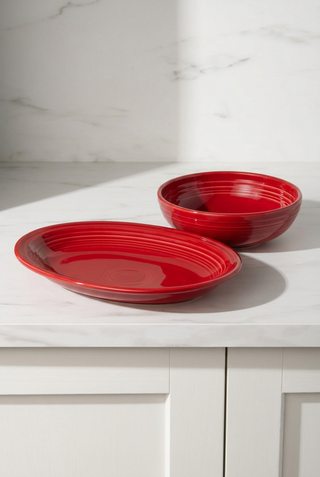 A red Large Oval Platter and a matching red Large Bistro Coupe Bowl with ridged detailing.