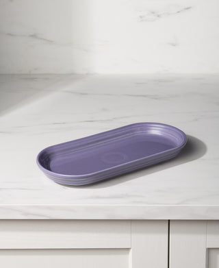 The Fiesta Lavender 11 7/8 Inch Oblong Serving Platter rests on a white marble countertop in a bright, modern kitchen.