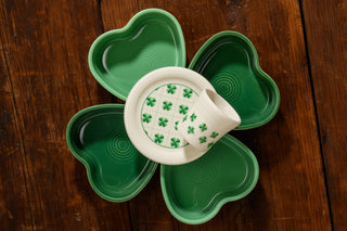Four green, heart-shaped Fiesta St. Patrick’s 4 3/8 Inch Coasters form a clover around a small white plate and mug cover, both adorned with green four-leaf clovers—a festive addition to any Fiesta collection or St. Patrick’s Day display.