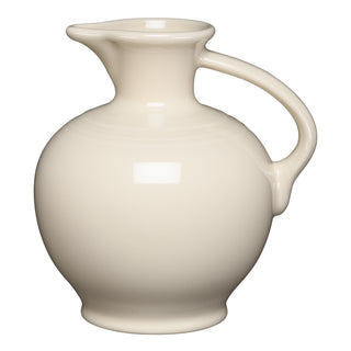 The Fiesta (FTC) Linen Carafe is a cream-colored ceramic pitcher with a round body, wide spout, and curved handle. Made in the USA, it's dishwasher safe and shown against a white background.