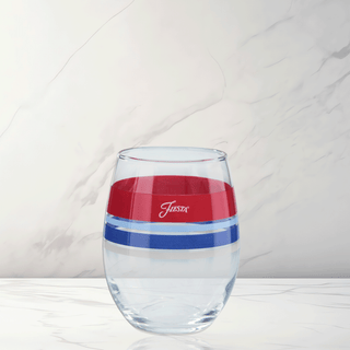A Moderne Glass Americana 15 oz. Edgeline Stemless Wine glass, set of 4, features red and blue horizontal stripes with "Fiesta" on the red stripe, displayed on a white marble surface with a light marble-patterned background.