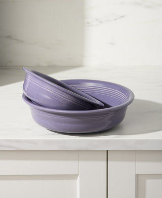 Two Fiesta Lavender Classic Rim 6 7/8 Inch Cereal Bowls (19 OZ) are stacked on a white marble countertop with gray veining, positioned in front of a white cabinet and marble-patterned backsplash.
