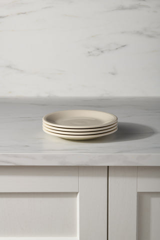The Fiesta (FTC) Linen Set of 4 Classic Rim 7 1/4 Inch Salad Plates is neatly stacked on a marble countertop in front of a white paneled cabinet and a light marble-patterned wall.