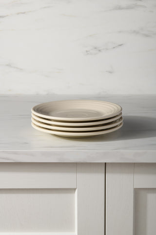 A stack of four Fiesta Linen Classic Rim 9 Inch Luncheon Plates, made in the USA, sits on a white marble countertop above a matching cabinet and light marble-patterned wall.