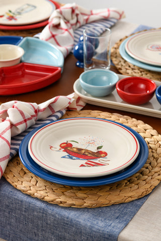 Set a festive table with the Fiesta Americana Apple Pie Classic Rim 9 Inch Luncheon Plate, featuring a patriotic apple pie design, paired with blue and red bowls, glassware, and a red, white, and blue napkin for a classic celebration.