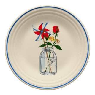 The Fiesta Americana Mason Jar Classic Rim 9 Inch Luncheon Plate features a cream color, blue rim, and a mason jar design with patriotic florals and pinwheel—ideal for adding Americana charm to your table.