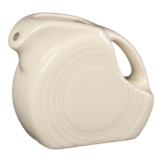 The Fiesta Linen 5 OZ Mini Disk Pitcher features a rounded art deco design, circular ridges, a built-in handle, and a small spout. Its cream shade and vibrant style make it a classic creamer inspired by Fiesta's iconic colors.