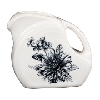 The Fiesta Botanical Floral Black 5 OZ Mini Disk Pitcher is a white ceramic piece with a curved handle and spout, accented by a black botanical floral design. It’s part of the Botanical Floral Dinnerware collection.