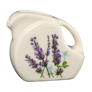 The Fiesta Lavender Bloom 5 OZ Mini Disk Pitcher is a cream-colored ceramic collectible serveware piece, featuring a curved handle, small spout, and beautifully painted purple lavender flowers with green stems and leaves on its side—expertly made in the USA.