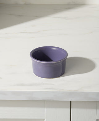 The Fiesta Lavender 8 OZ Ramekin (4 Inch) is a small, round, purple ceramic dish sitting on a white marble countertop, providing an oven-safe solution for your baking needs.