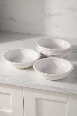 The Fiesta (FTC) White Set of 4 Classic Rim 8 3/8-Inch, 34OZ Pasta Bowls are stacked on a marble countertop in a bright kitchen. These dishwasher-safe bowls combine style and practicality for your dining experience.