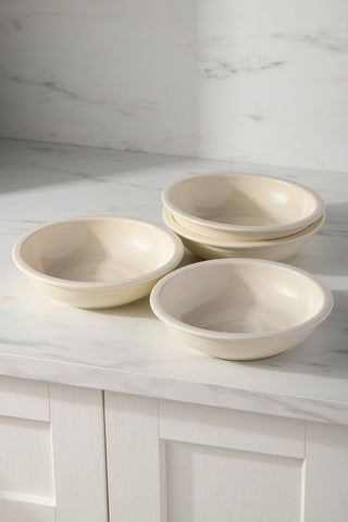 Four Linen Fiesta (FTC) Classic Rim 8 3/8-Inch 34oz Pasta Bowls are stacked on a white marble countertop, showcasing this elegant, lead-free ceramic 4-piece set against white cabinets and a light marble backsplash.