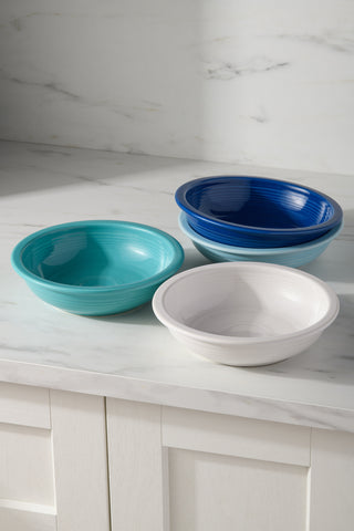 A set of four Fiesta (FTC) Mixed Coastal Blues Classic Rim 8 3/8-Inch 34OZ pasta bowls in teal, blue, and white are arranged on a marble countertop. These dishwasher safe bowls combine style and convenience for everyday dining.