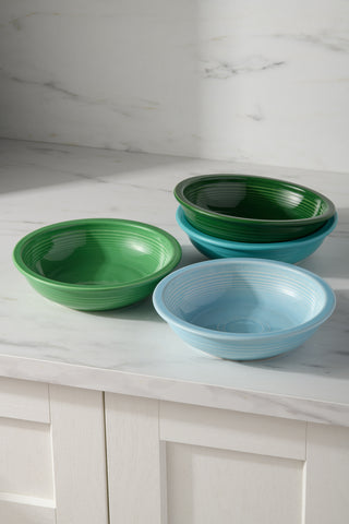 Four Fiesta Mixed Aegean Classic Rim 8 3/8-Inch 34oz Pasta Bowls in green and blue sit stacked on a white marble countertop above a light cabinet. This lead-free ceramic set of four is stylish and safe for dining.