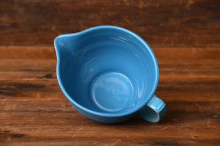 A Fiesta Factory Direct Peacock Batter Bowl in the retired Peacock color, featuring a handle and pouring spout, sits on a wooden surface and is viewed from above.