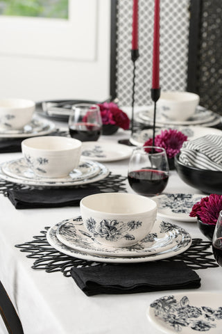 A dining table set with the Fiesta Factory Direct Botanical Floral Black Classic Bistro 3-piece Place Setting, black napkins, red wine glasses, dark pink flowers, and tall red candles creates an elegant and sophisticated atmosphere.